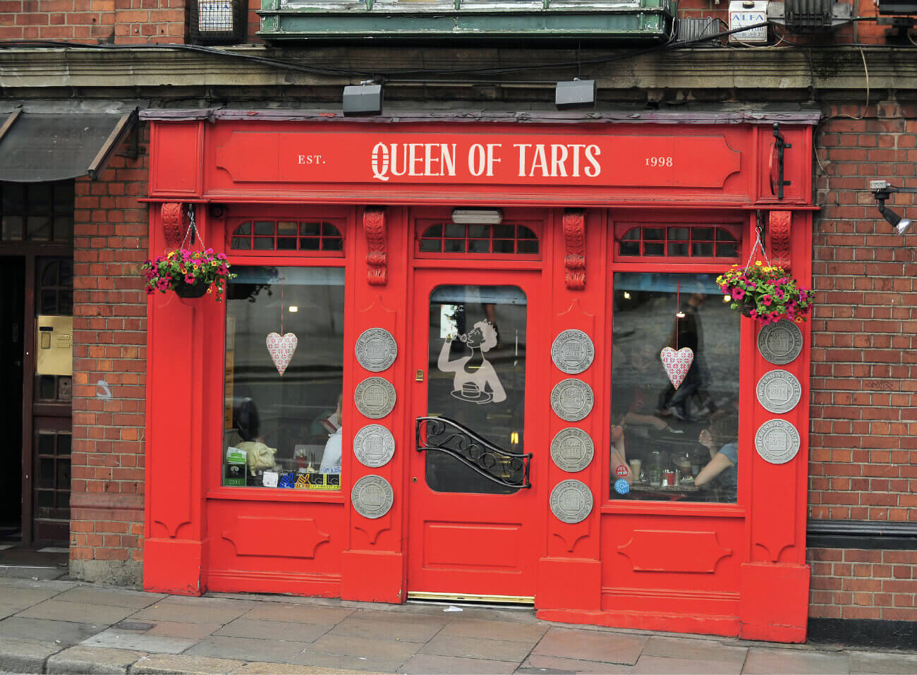 Rote Ladenfront des Queen of Tarts Café in Dublin mit neuem Schriftzug und Bildmarke auf Fenster und Beschilderung — fiktives Restaurant Branding von NOVA & BOW